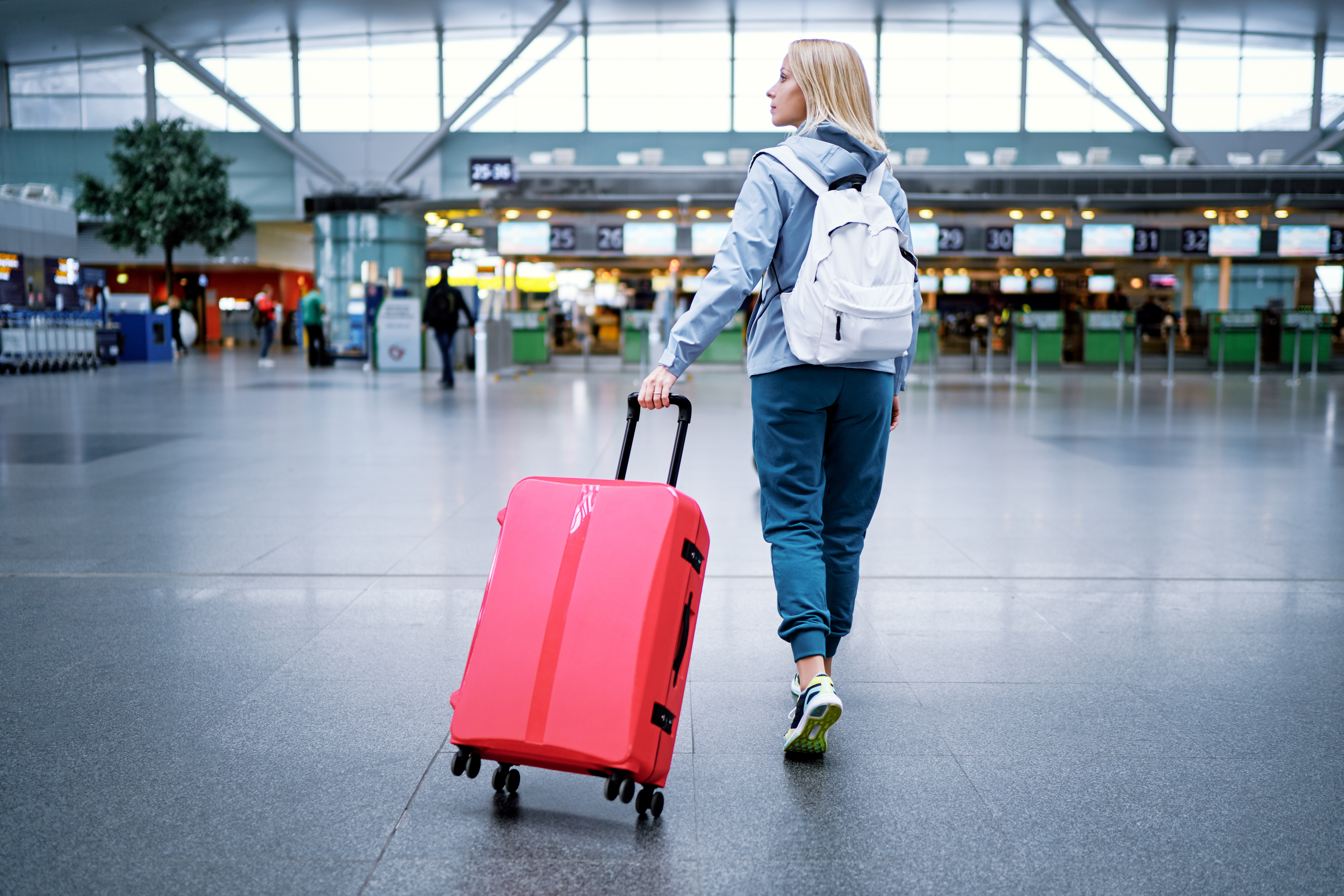 Eine Frau mit blonden Haaren, die einen roten Koffer in einem Flughafen hinter sich herzieht.