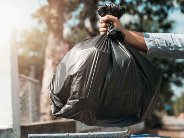 schwarzer Müllsack wird in eine Mülltonne geworfen